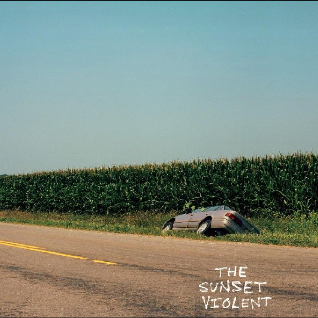 Car on its side on a road next to a cornfield with 'The Sunset Violent' text.