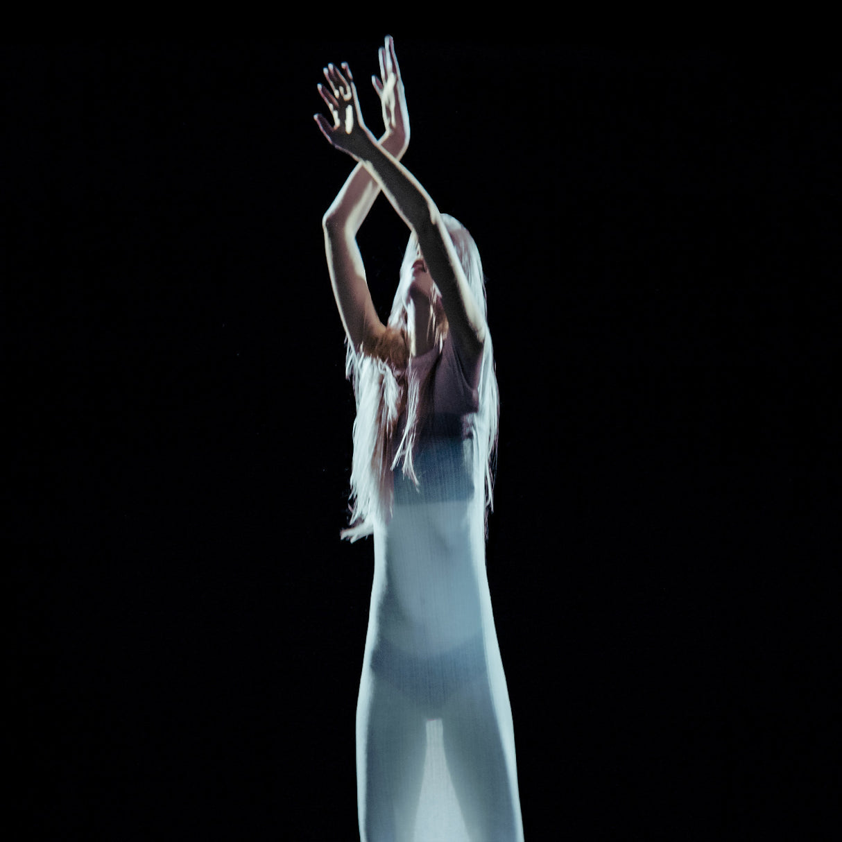 Person with long hair and white pants reaching upwards against a black background
