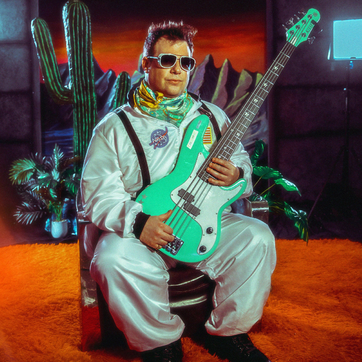 Person in astronaut suit holding a green bass guitar with desert landscape background