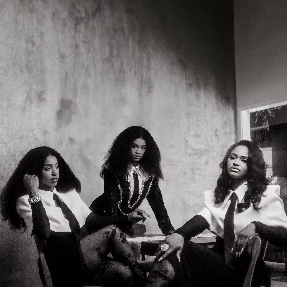 Black and white photo of three women sitting together in a room with a textured wall.