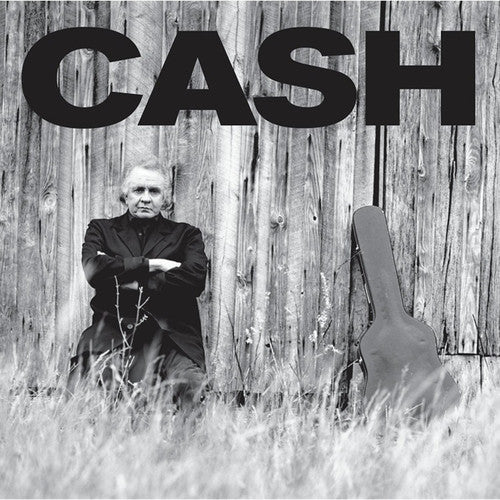 Black and white image of a person sitting against a wooden fence with the word 'CASH' above, and an acoustic guitar leaning against the fence.