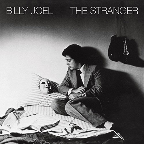 A black and white album cover of Billy Joel titled 'The Stranger' with a image of Billy Joel sitting and holding a mask.