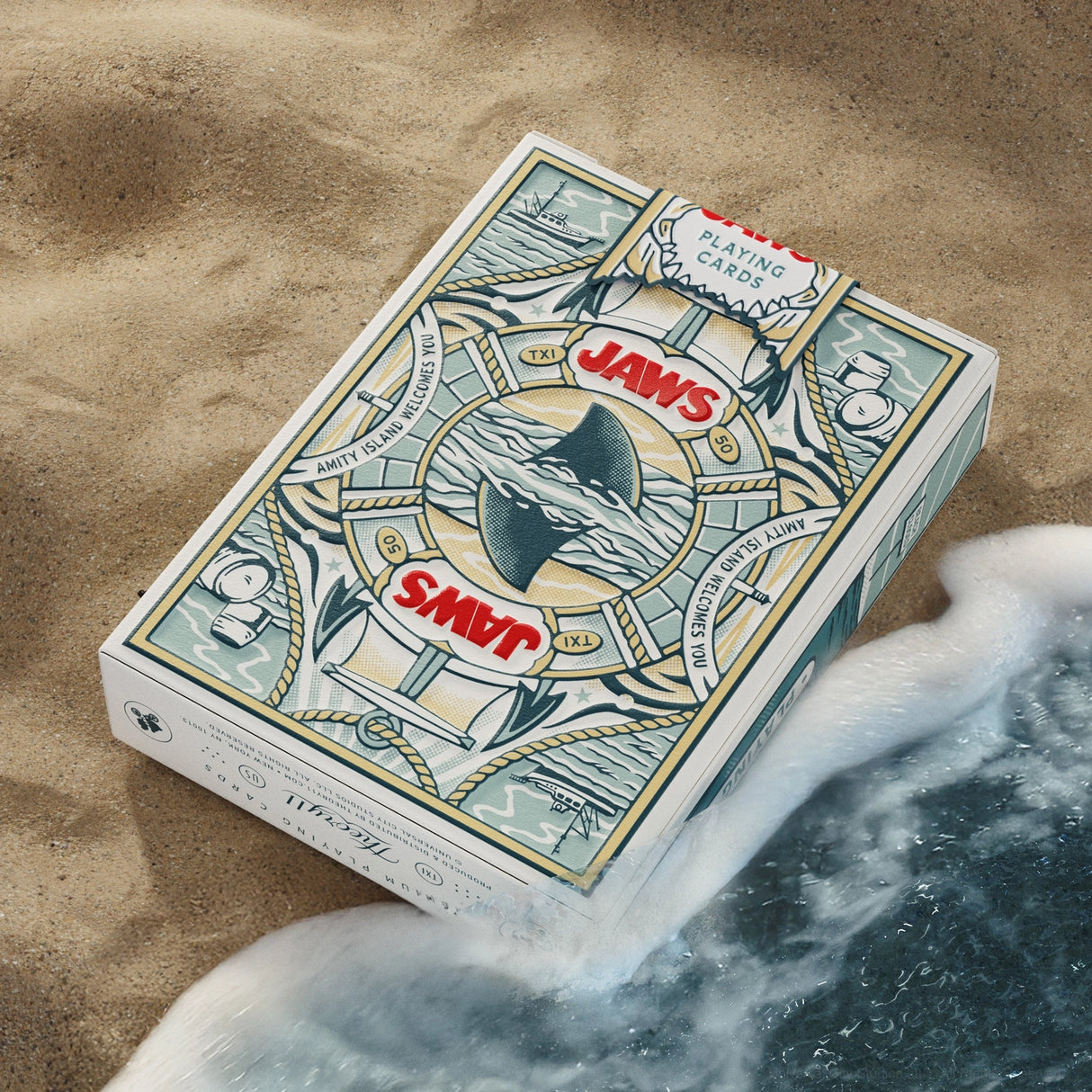Jaws-themed playing card box on sand with ocean wave