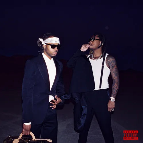 Two men standing in a desert-like setting at night, with one man holding a CD case and the other adjusting his tie. Both are wearing sunglasses and black suits.
