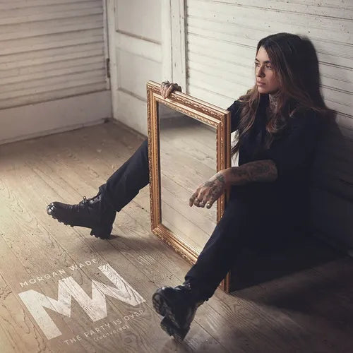 Person sitting on the floor with a large mirror, album cover with 'M' logo