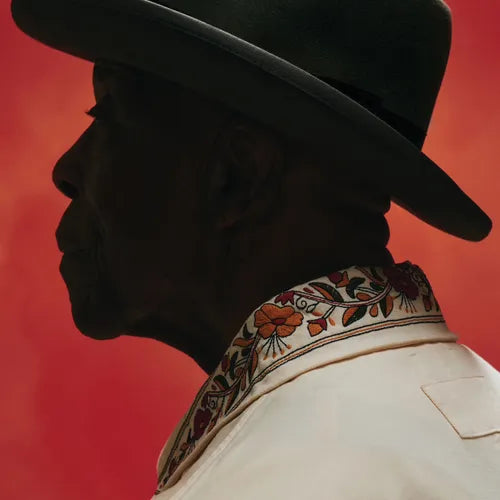Silhouette of a person wearing a wide-brimmed hat and embroidered garment against a red background