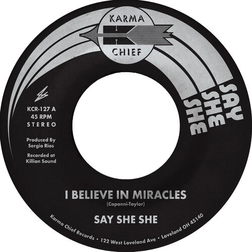 A 7-inch vinyl record label for 'I Believe In Miracles' by Say She She, with a black background and white text, released under the Karma Chief label.