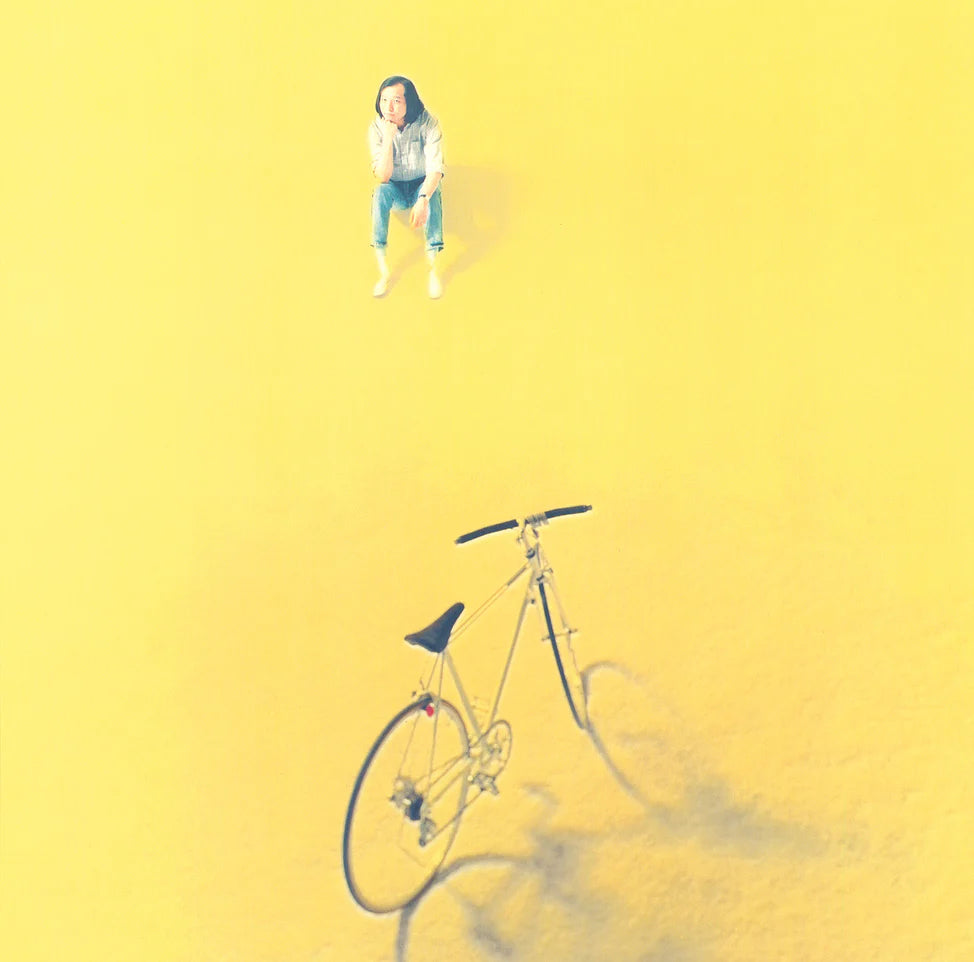 Person sitting on a bicycle against a yellow background