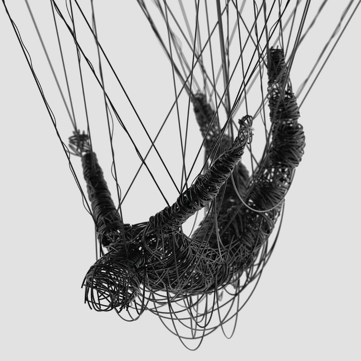 A black wire sculpture of a human figure suspended upside down by multiple thin strings against a light gray background.