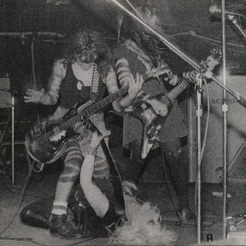 Two musicians playing electric guitars on stage with a microphone stand in the foreground.