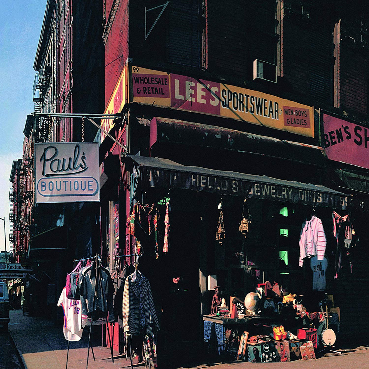 Street view of a clothing store with various signs and hanging clothes.