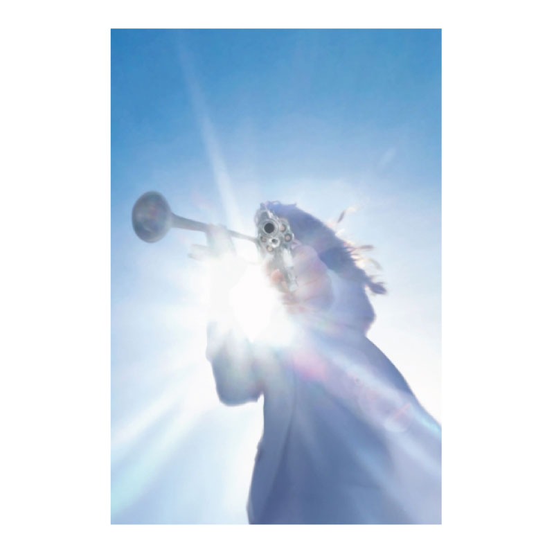 Person holding a trumpet against a bright blue sky with lens flare