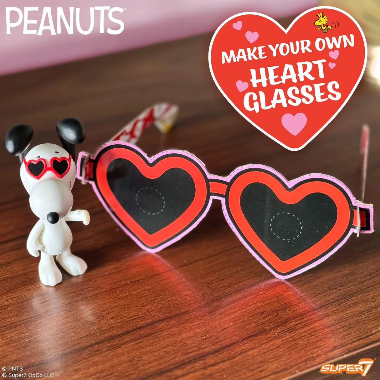 Heart-shaped glasses with a Snoopy figure and promotional text on a wooden surface.