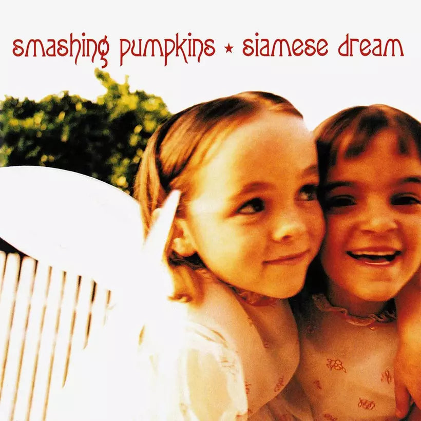 The image displays the cover art for the Smashing Pumpkins' album 'Siamese Dream.' It features a soft-focus, warm-toned photograph of two young children smiling and sitting close to each other, adding a playful and innocence-themed aesthetic to the album cover.