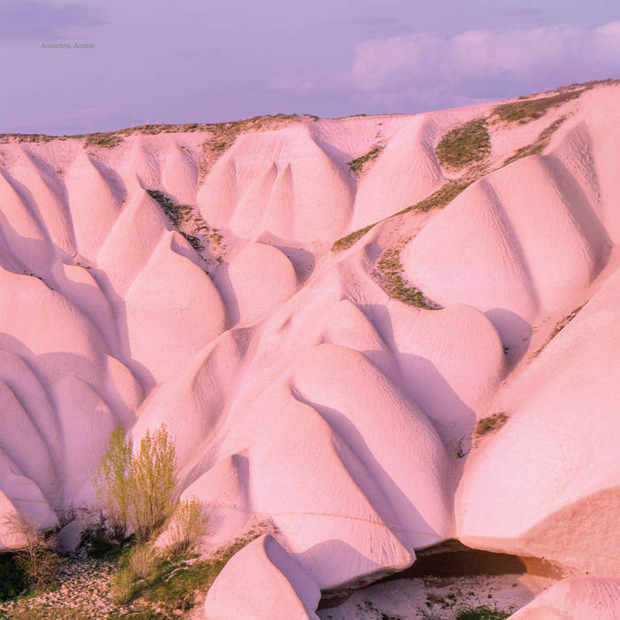 Wavy pink rock formations with sparse greenery under a purple sky.