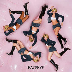 Five stylized fashion photos of a blonde model posed on a pink satin-like surface, wearing dark blazers, denim skirts, white bralettes, and black knee-high boots. The word 'KATSEYE' appears at the bottom.