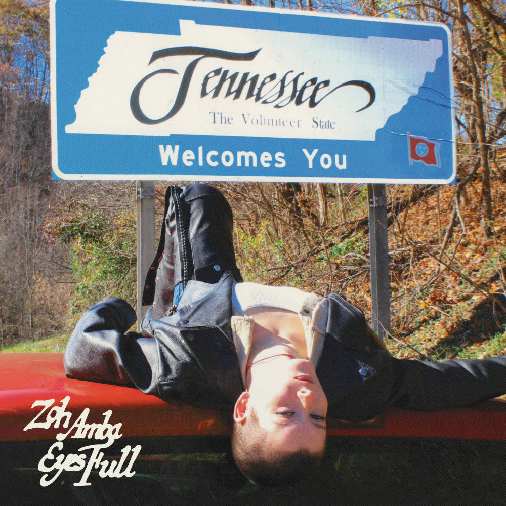 Person lying on a car hood with 'Tennessee Welcomes You' sign in the background