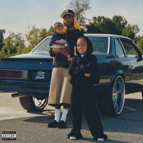 Man holding a child and standing next to another child in front of a blue car on a road.
