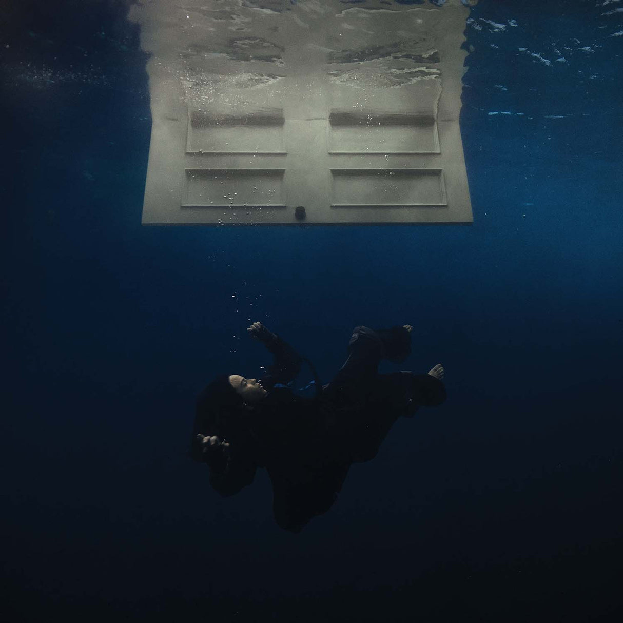 Person underwater with a door above in a pool