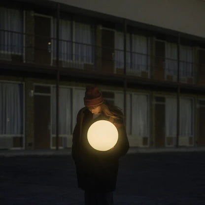 Person holding a glowing round object in front of a building at night