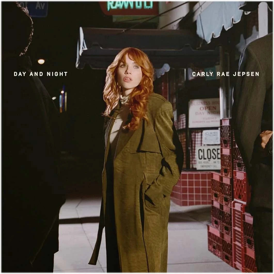 Album cover for Carly Rae Jepsen's 'Day and Night', featuring the artist standing on a city street at night wearing an olive green trench coat.