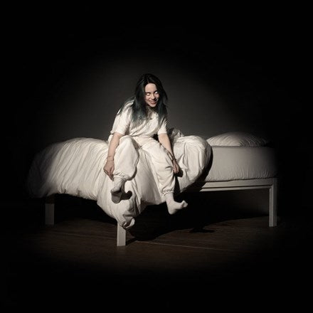 Billie Eilish sitting on a bed in a white outfit, with the album cover displaying the text 'When We All Fall Asleep, Where Do We Go?'.