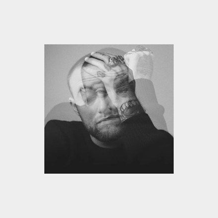 A black and white image of Mac Miller with his hands clasped in front of his face. He is wearing a sweater and has tattoos visible on his arms.