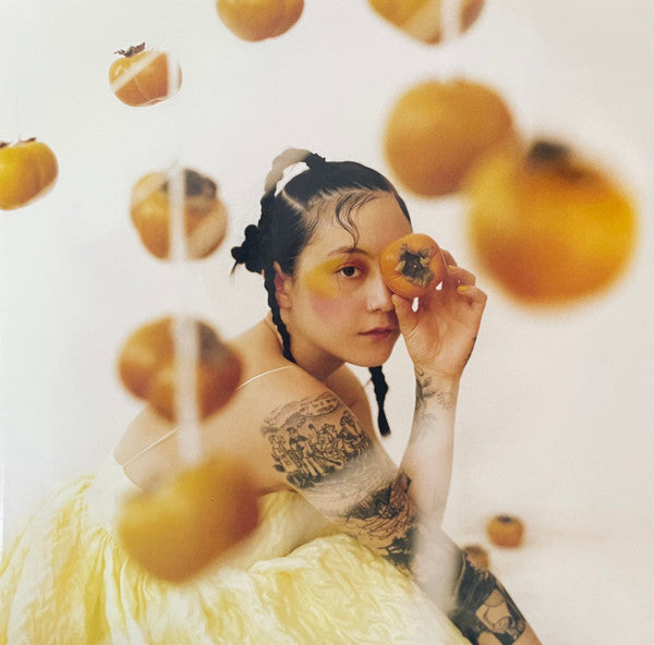 A person with a tattoo on their arm holding a tomato, surrounded by multiple tomatoes in the air, all against a white background.