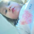 A close-up lifestyle shot of a young child wearing a white knit sweater with a pink heart pattern and blue lettering, photographed in a soft, heavily filtered light.