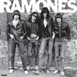 Black and white photo of the band Ramones standing against a brick wall with large white RAMONES lettering across the top.