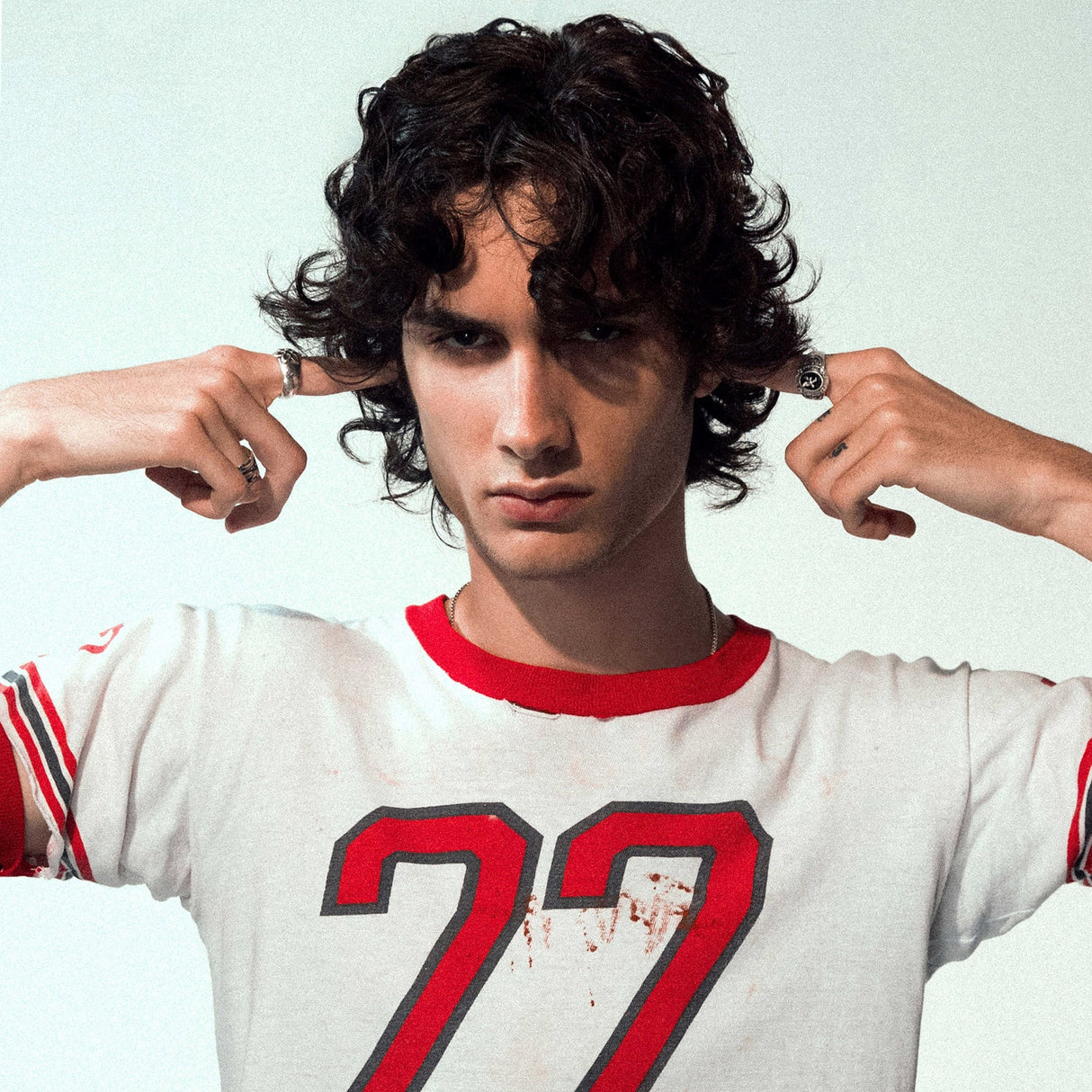 Person wearing a white jersey with red accents and the number 27, posing with hands on head.