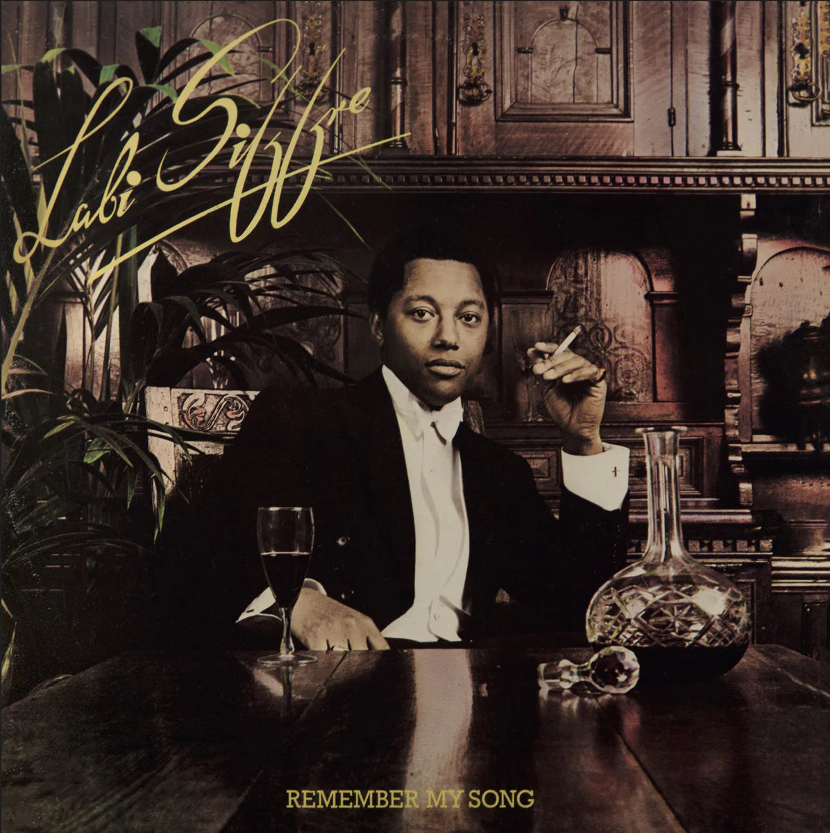 Album cover with a person sitting at a table with a glass and decanter, surrounded by decorative items.