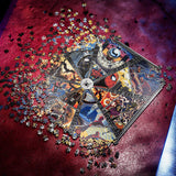 A partially assembled multicolor jigsaw puzzle featuring comic book-style artwork, photographed from above on a textured red surface with loose puzzle pieces scattered around it.