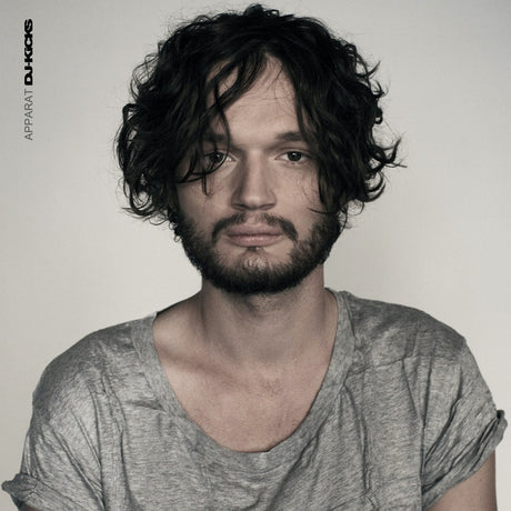 Man with wavy hair and beard wearing a gray shirt against a plain background