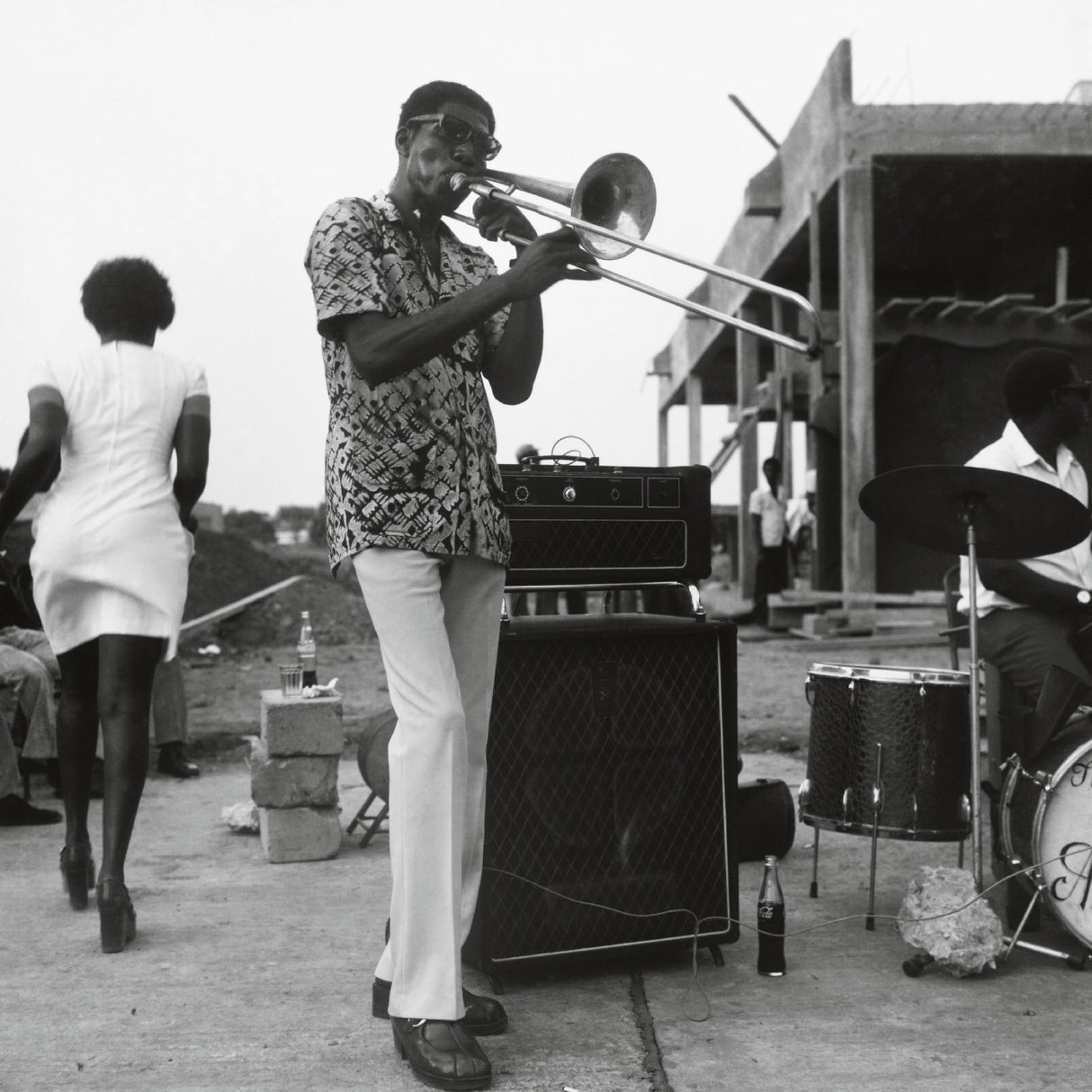 Man playing trombone outdoors with a band and audience in the background