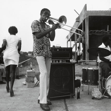Man playing trombone outdoors with a band and audience in the background