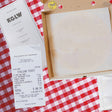Open pizza box with a printed menu and receipt on a red and white checkered tablecloth.