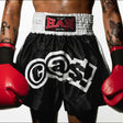 Person wearing black boxing shorts with white logos and red boxing gloves, on a plain background