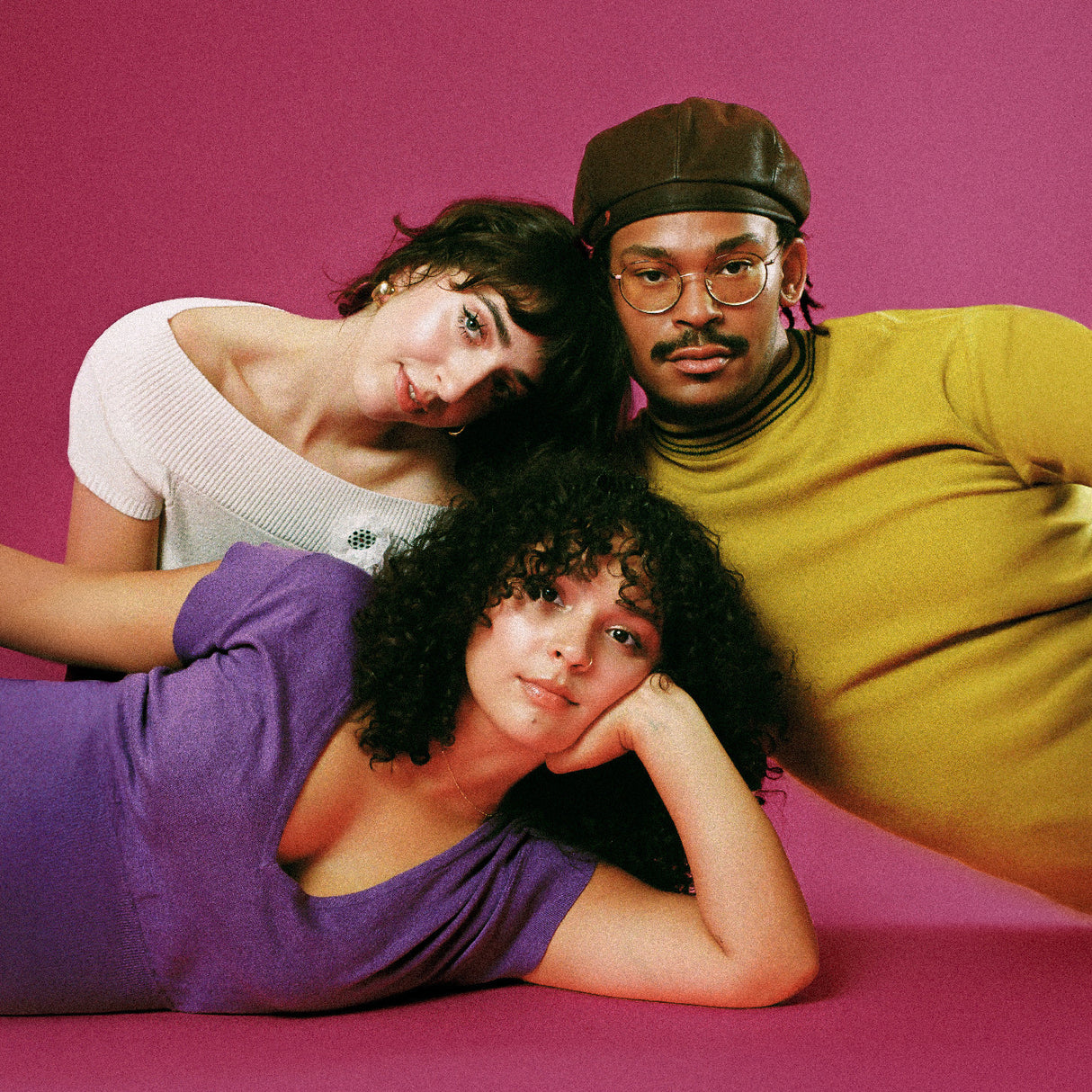 Three people posing together against a pink background