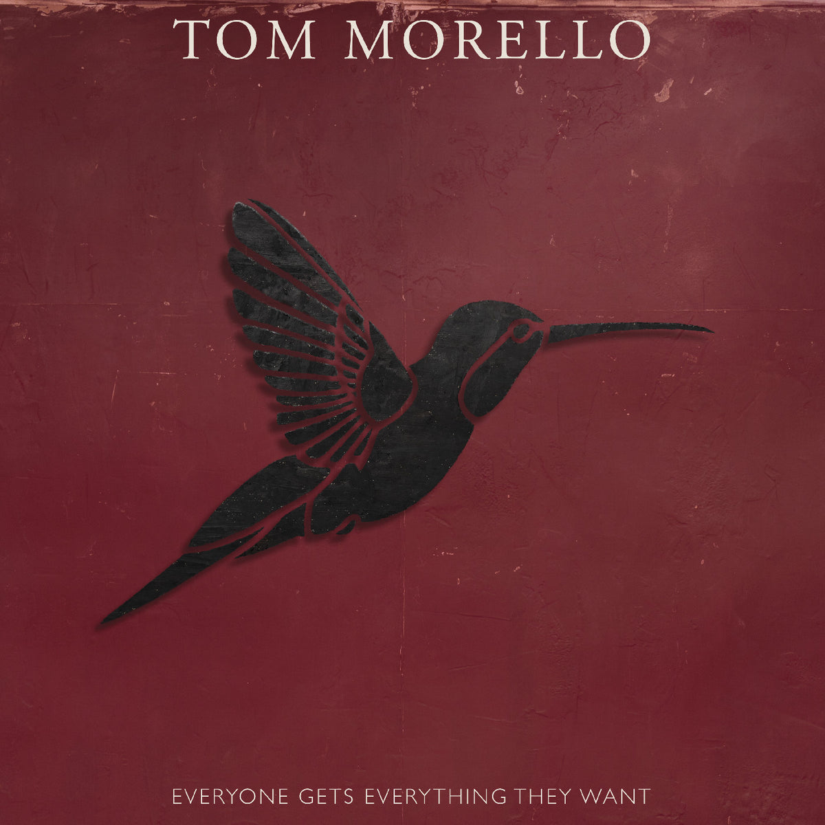 Album cover for Tom Morello's 'Everyone Gets Everything They Want', featuring a dark silhouette of a hummingbird on a textured dark red background with the artist's name at the top and the album title at the bottom.