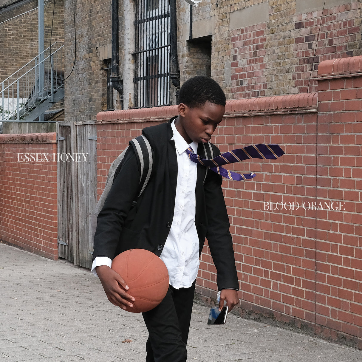 Person holding a basketball against a brick wall with 'Essex Honey' and 'Blood Orange' branding.