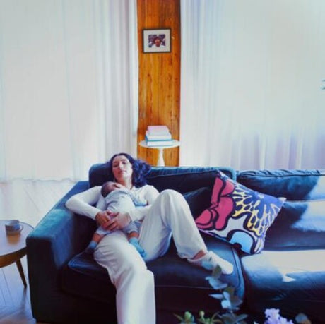 A person sitting on a couch holding a baby, with a pillow behind them featuring a colorful, abstract design.