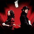 Two people in formal attire with a microphone and red background