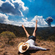Person lying on their back with legs in the air, wearing a hat, with a volcanic eruption in the background.