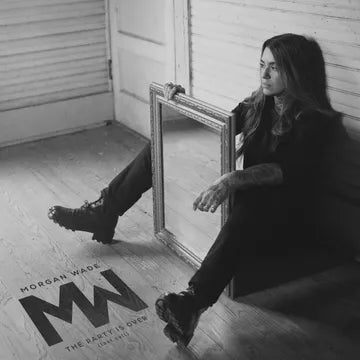 Person sitting on a wooden floor with a large mirror behind them, wearing a black outfit.