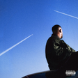 Person sitting on a car with a clear blue sky and contrails in the background