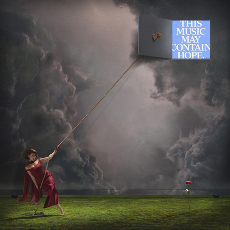 Woman in a red dress holding a kite with 'This Music May Contain Hope' text against a stormy sky.