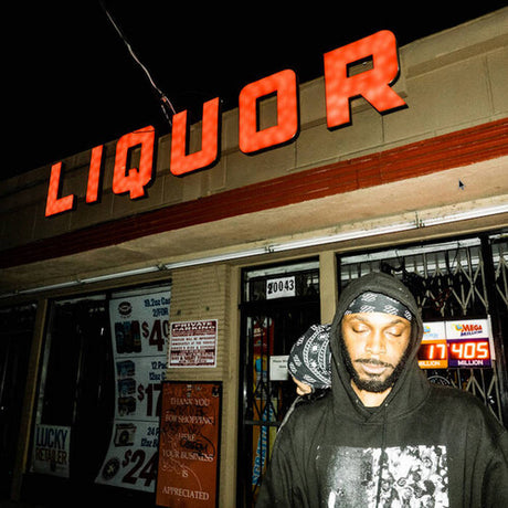 A person standing in front of a liquor store at night, wearing a hoodie with a graphic design.