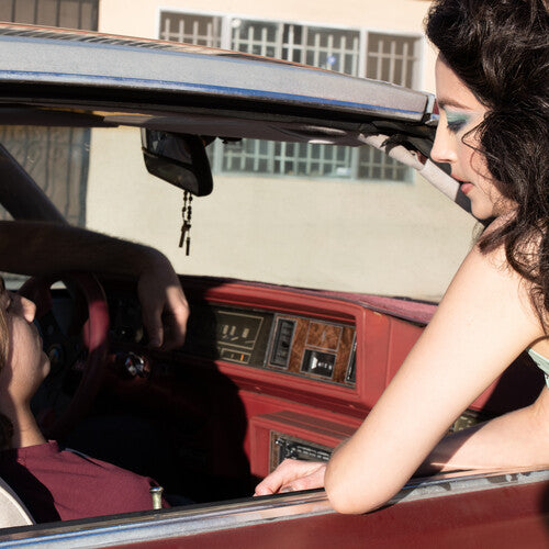 Woman sitting in a vintage car with a man outside, looking into the car.