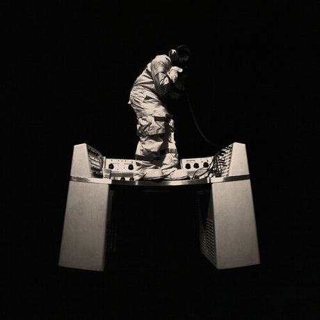 Person in a protective suit standing on a large metallic object against a black background